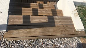 Une terrasse en bois mène à une porte blanche dotée d’un panneau de verre.