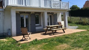 Une maison à deux étages dotée d’un balcon, d’une terrasse en bois et d’un patio aménagé avec une table et des chaises.