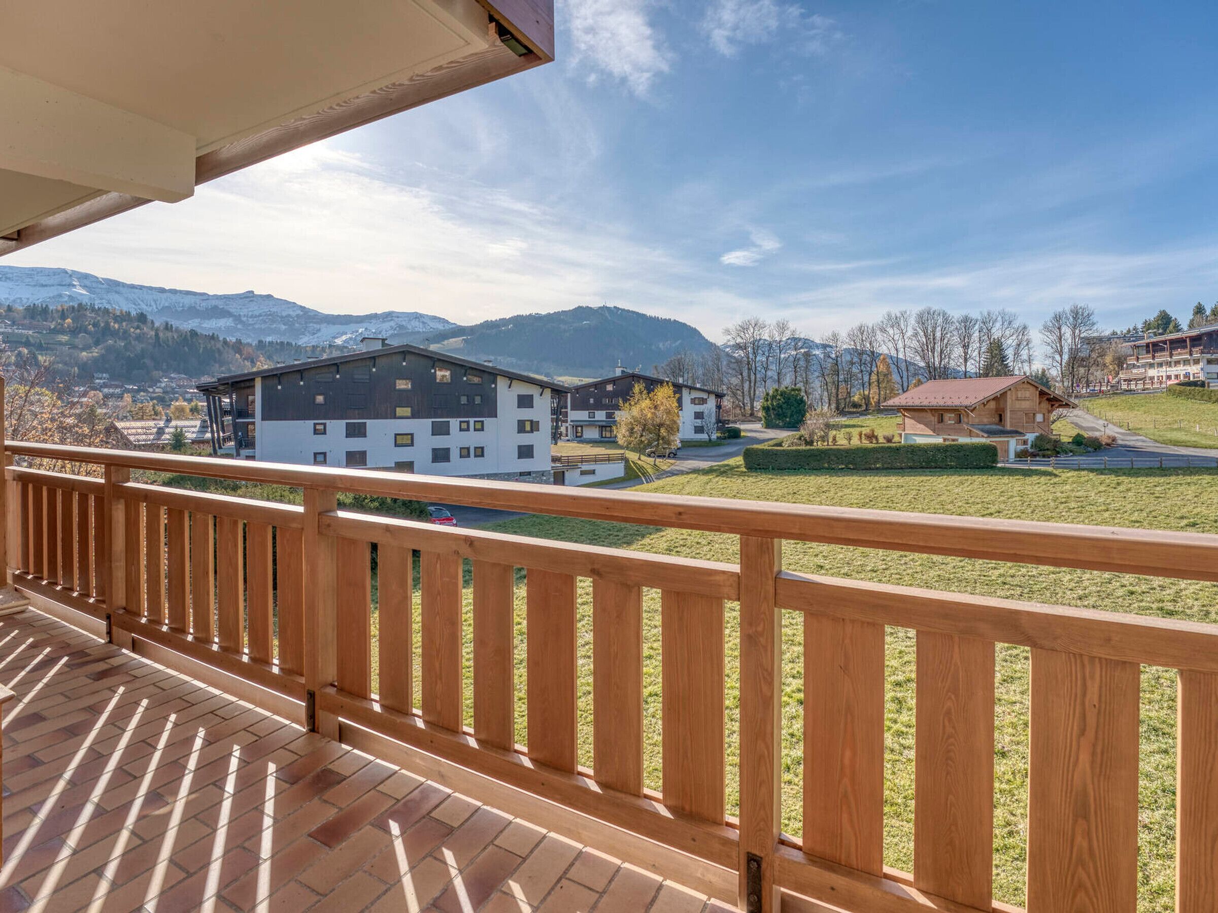 A wooden balcony with a view of a mountain landscape, including buildings and a clear sky.