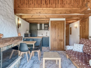 A cozy interior with a wooden ceiling, a dining area with chairs, a sofa with patterned cushions, and a kitchen with cabinets and a sink.