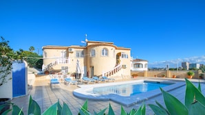 Une grande maison avec une piscine, de nombreux fauteuils et des plantes en pot.