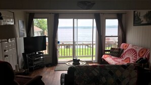 A living room with a television, a sofa, and a view of the water. - PEACEFUL OASIS COTTAGE (Keene)