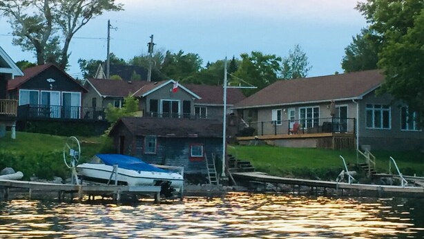 A waterfront property with houses, a dock, and a boat. - PEACEFUL OASIS COTTAGE (Keene)