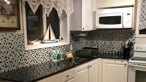 A kitchen with white cabinets, a black countertop, a microwave, and a stove. - PEACEFUL OASIS COTTAGE (Keene)
