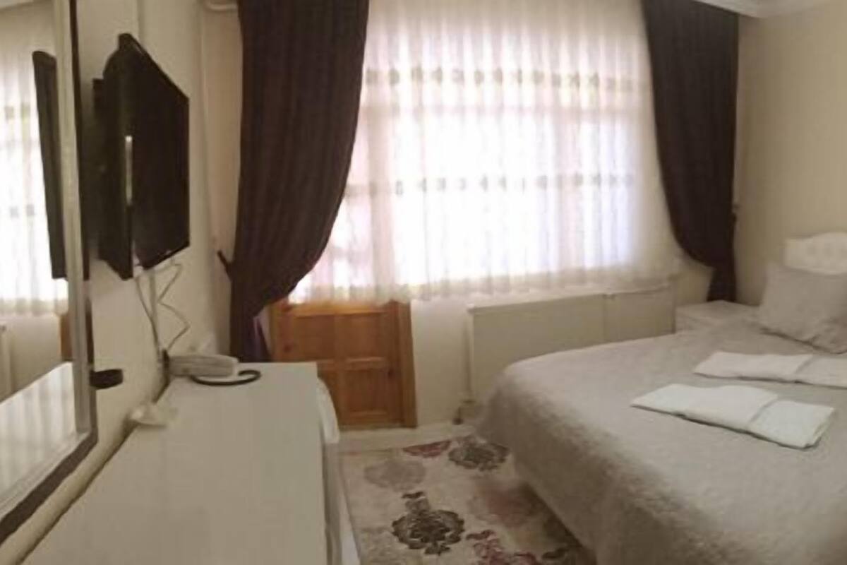 Une chambre à coucher avec un lit, une table de chevet, un miroir et une fenêtre avec des rideaux.