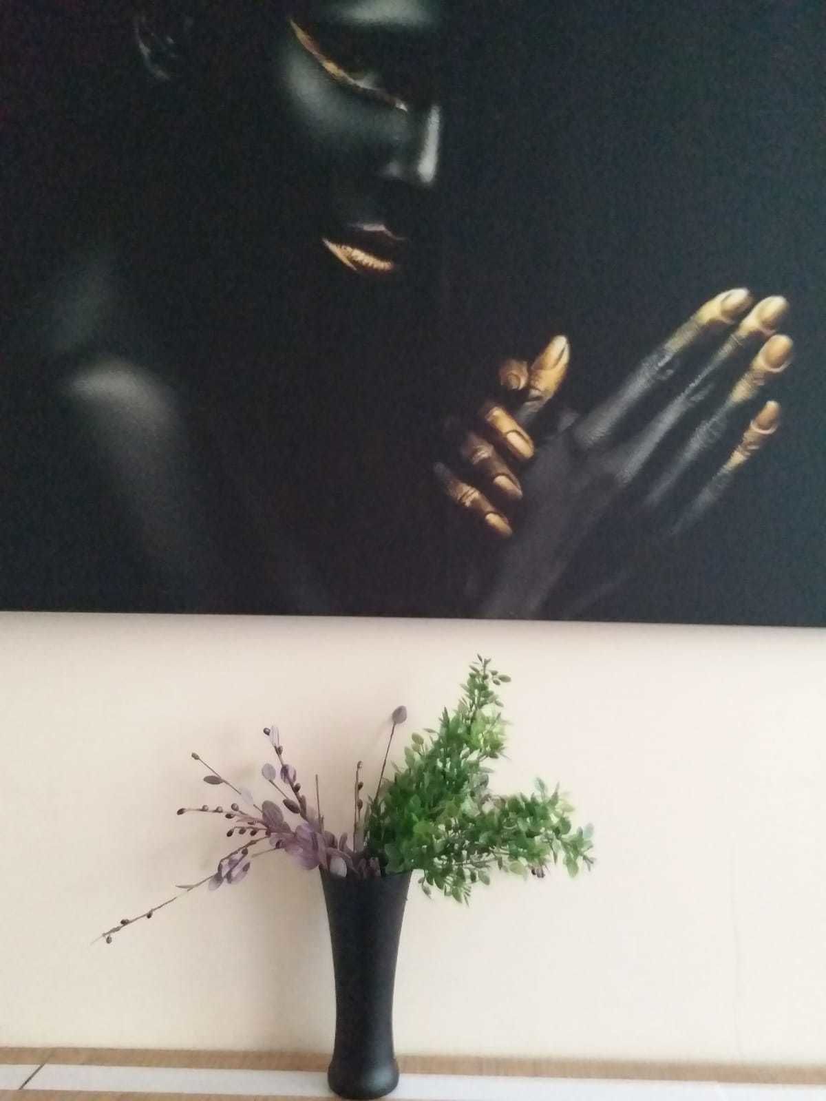 Una pintura que muestra a una persona con la mano extendida, un florero con plantas verdes y moradas sobre una mesa.