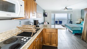 A modern kitchen with wooden cabinets, a built-in microwave, and a stove. There is a dining area with a view of the ocean.