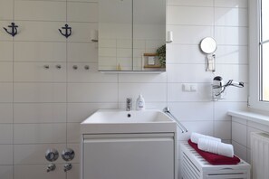 A bathroom with a white sink, a mirror, a towel rack, and a towel dispenser. - Centrally located apartment for 4 people, south-west facing terrace, washing machine, WLAN (Ostseebad Prerow)