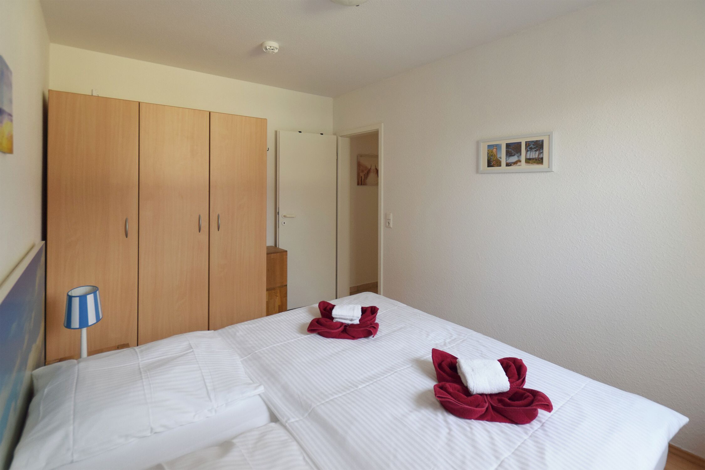 Ett hotellrum med två sängar, en garderob, en lampa och en liten inramad tavla på väggen.