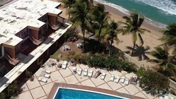 A beachfront hotel with a pool, lounge chairs, and palm trees. - Beach front, best location, ocean and city views + parking! (San Juan)