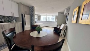 A modern kitchen with white cabinets, a dining table with chairs, and a view of the city through large windows. - Beach front, best location, ocean and city views + parking! (San Juan)