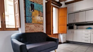 A modern kitchen with white cabinets, a grey sofa, and a brick wall with a colorful painting. - Flats Friends Tetuan Studio (Valencia)
