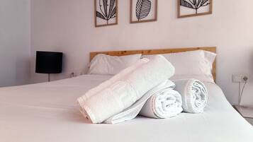 A neatly made bed with rolled white towels, a wooden headboard, and three framed leaf artworks on the wall.
