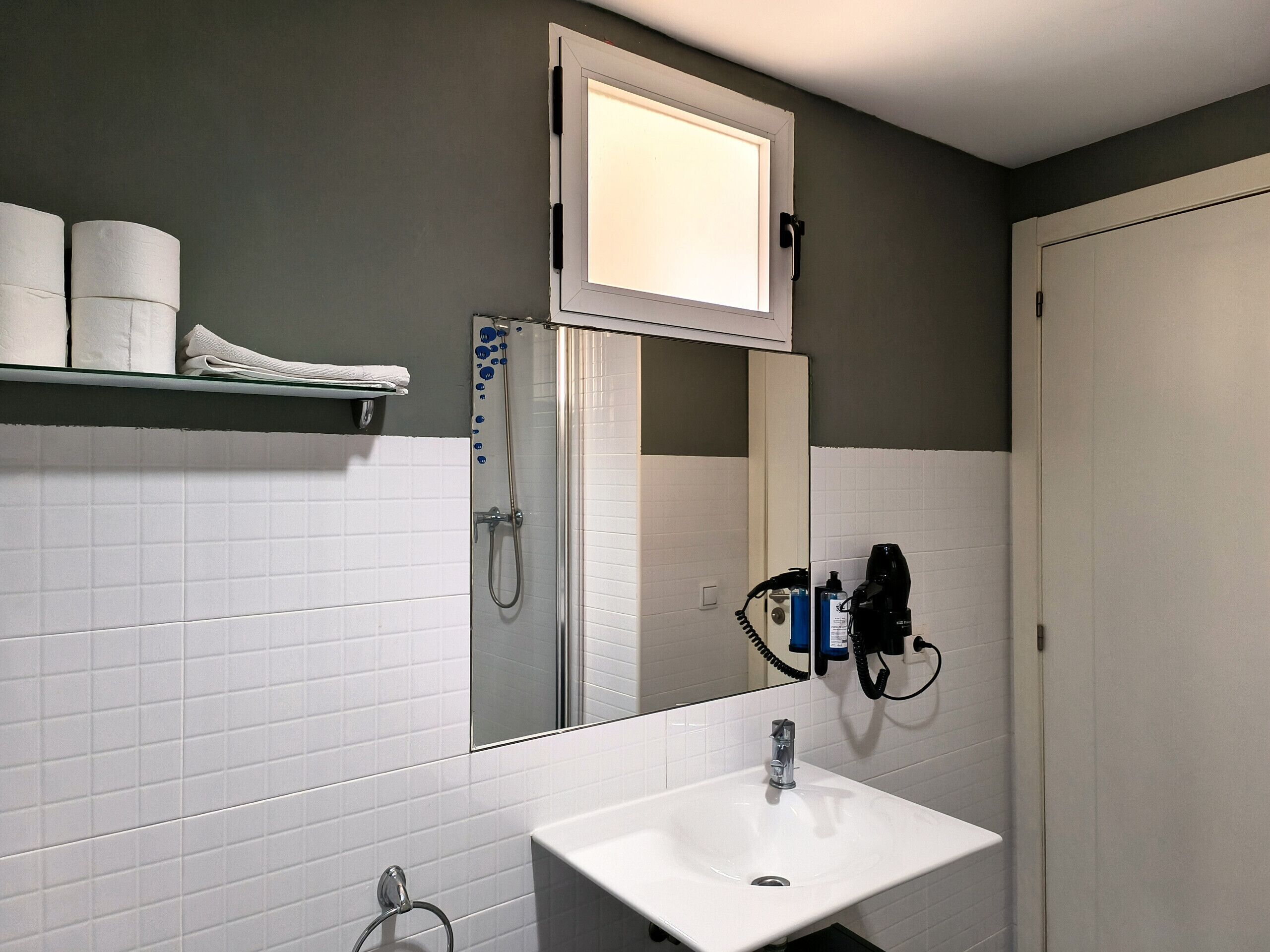 A bathroom with a white sink, a glass shower enclosure, a towel rack with towels, and a mirror above the sink.