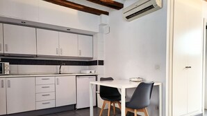A compact kitchen with white cabinets, a white countertop, a small sink, and a dining area with two chairs. - Flats Friends Tetuan Studio (Valencia)