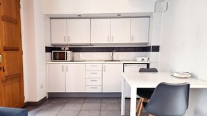 A compact kitchen with white cabinets, a microwave, a sink, and a dining area with a table and chairs. - Flats Friends Tetuan Studio (Valencia)