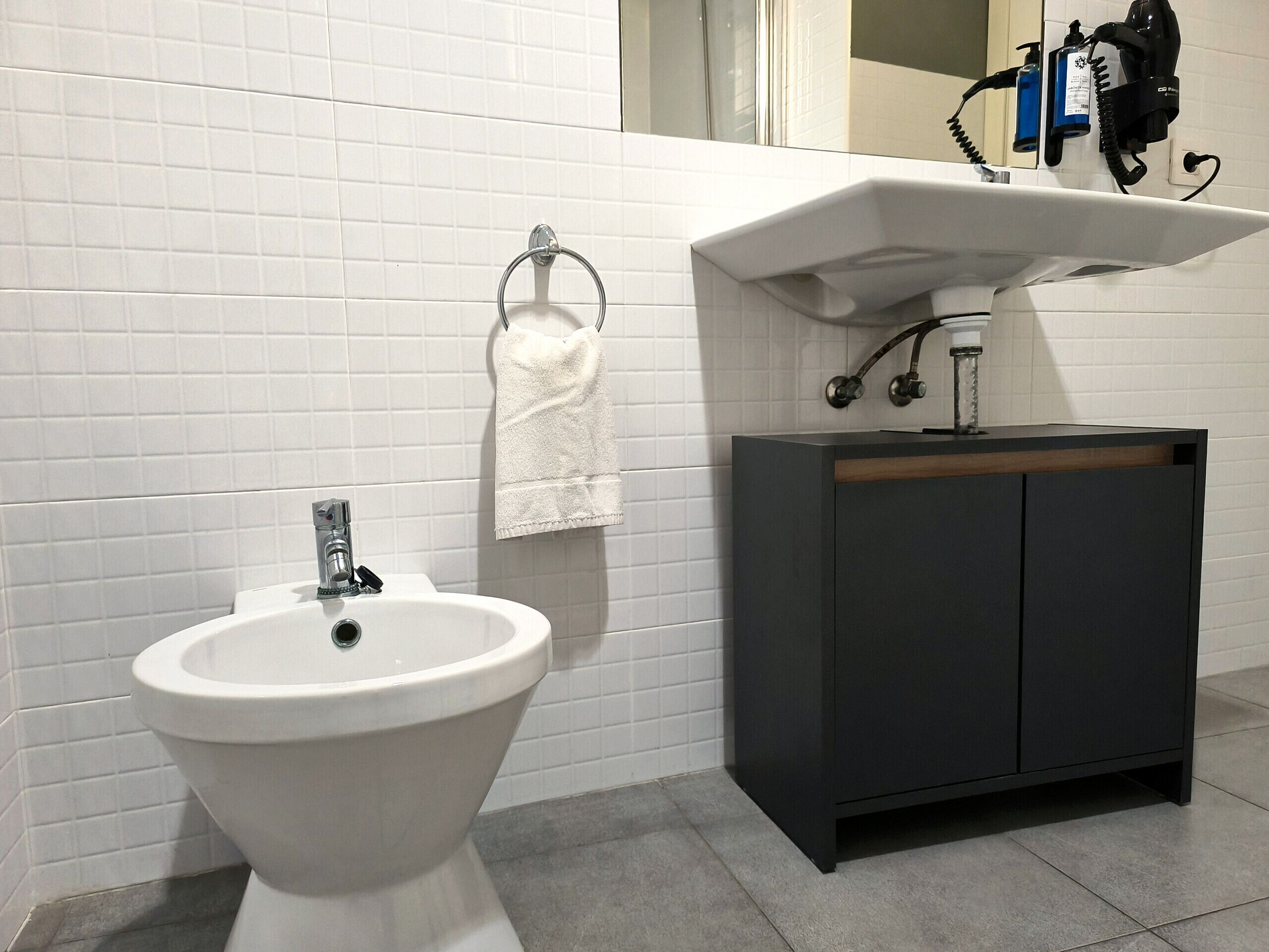 Une salle de bain moderne avec un bidet sur pied blanc, un meuble-lavabo en bois foncé et une serviette blanche suspendue à un anneau en métal.