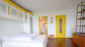 A bedroom with a bed, a wooden floor, a yellow door, and a white wardrobe. - Spacious Apartment in Evian with Lake View, Balcony, and Pet-Friendly (Évian-les-Bains)