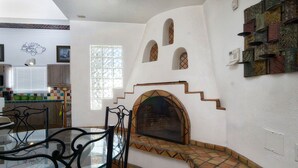 A dining area with a glass table and chairs, a fireplace with a brick surround, and a window with a geometric pattern.