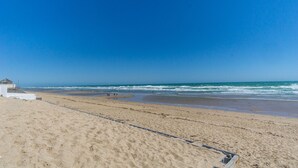 A beach with a clear sky, sandy shore, and a small building with a thatched roof.
