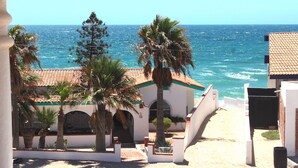 A coastal building with a tiled roof, palm trees, and a view of the sea.