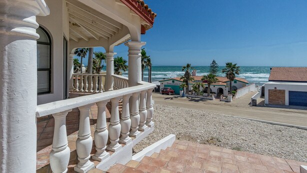 A beachfront property with a balcony, palm trees, and a view of the ocean.