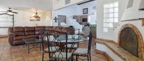 A spacious living area with a brown leather sofa, a glass-top dining table with chairs, and a kitchen in the background.