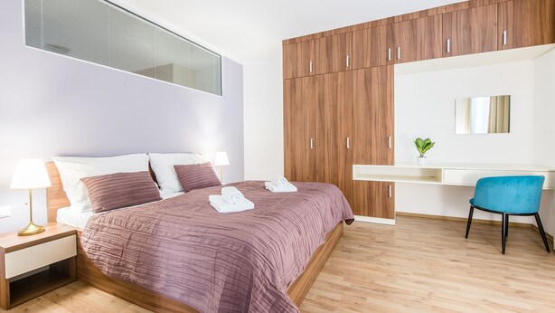 Un dormitorio moderno con cama, mesita de noche, lámpara, armario de madera, escritorio, silla y una planta en maceta.
