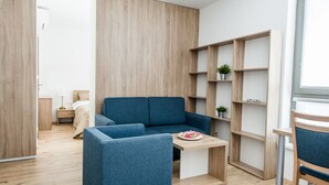 Una habitación moderna y funcional con un sofá azul, una pequeña mesa de madera con un plato de comida y una estantería de madera empotrada.