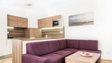 Una cocina moderna con armarios de madera y microondas integrado, un sofá morado y una mesa pequeña con un plato de comida.