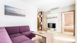 Una sala de estar moderna con un sofá seccional morado, una mesa de centro de madera, un televisor de pantalla plana y una estantería.