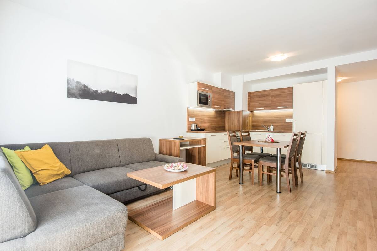 A modern living room with a grey sofa, a small wooden coffee table, and a dining area with a wooden table and chairs.