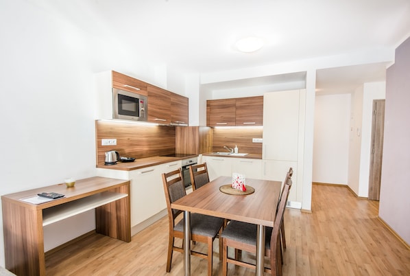 A modern kitchen with wooden cabinets, a built-in microwave, and a dining area with a wooden table and chairs. - Apart Hotel VIRGO (Bratislava)