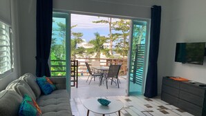 Een woonkamer met een bank, een salontafel en een televisie. Er is een schuifdeur die leidt naar een terras buiten met een tafel en stoelen.