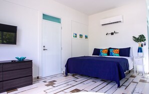 A bedroom with a bed, a dresser, a TV, an air conditioner, and a door. - ★ Happy Turtle Loft - Sparkling clean corner loft steps to Sandy Beach ★ (Rincon)
