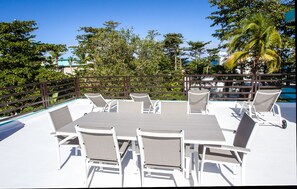A poolside area with a table and chairs, surrounded by a wooden fence and lush greenery. - ★ Happy Turtle Loft - Sparkling clean corner loft steps to Sandy Beach ★ (Rincon)