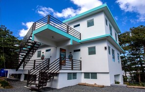 A multi-story building with a white exterior and teal accents, featuring a staircase with a metal railing leading to the upper levels. - ★ Happy Turtle Loft - Sparkling clean corner loft steps to Sandy Beach ★ (Rincon)