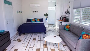 Een slaapkamer met een bed, een grijze bank, een witte salontafel, en een kitchenette op de achtergrond.