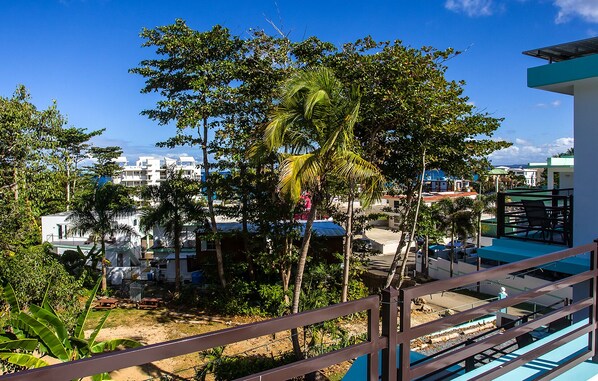 A residential area with a balcony overlooking a street, surrounded by trees and buildings. - ★ Happy Turtle Loft - Sparkling clean corner loft steps to Sandy Beach ★ (Rincon)