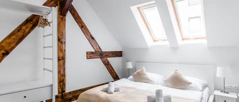 A bedroom with a sloped ceiling, wooden beams, a bed with white linens, two bedside tables, and a window.