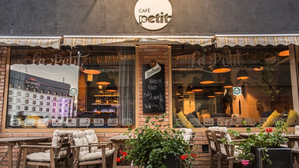 Een café met terras, een krijtbordmenu en een uitzicht op de stad door grote ramen.