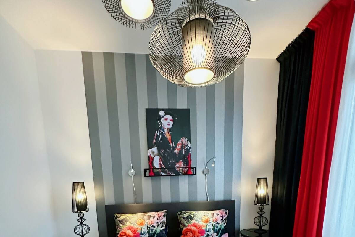 Un dormitorio con colcha estampada, papel tapiz a rayas y un cuadro en la pared.