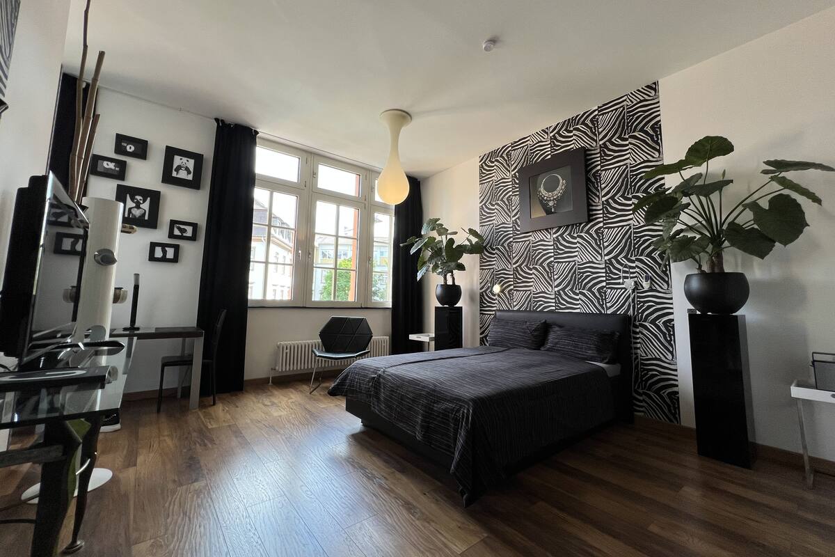 Un dormitorio con cama, escritorio, silla, radiador y una ventana grande.