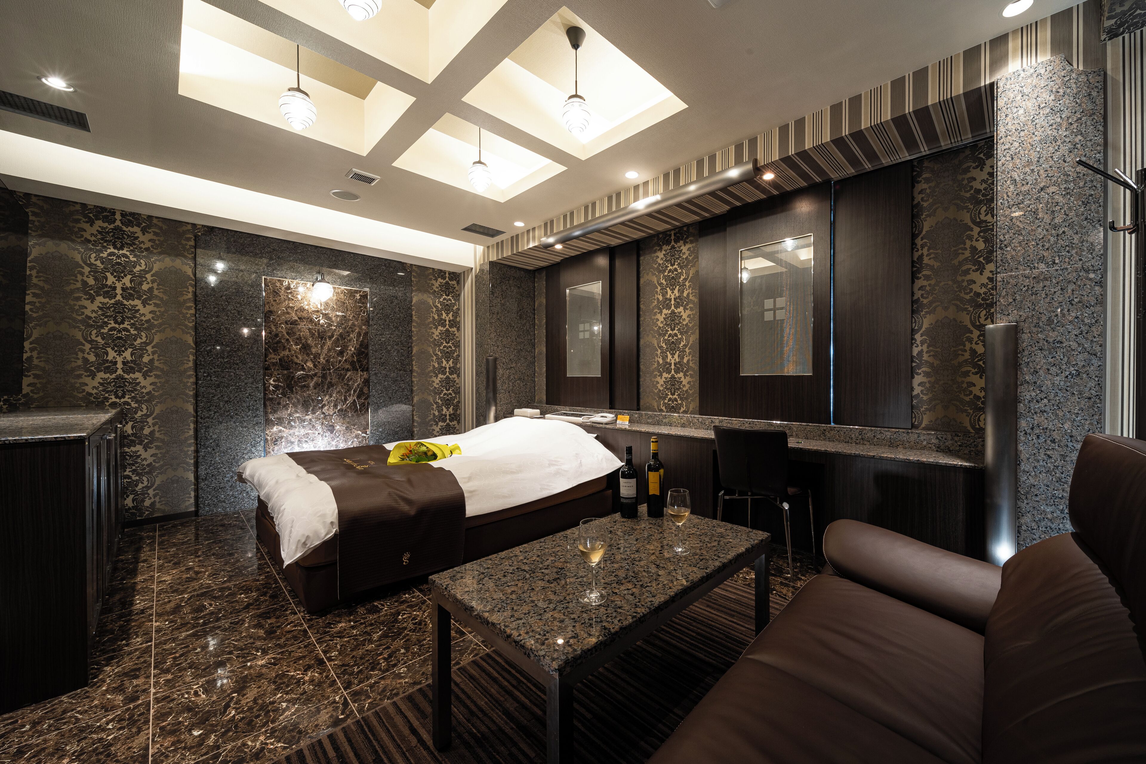A modern hotel room with a bed, a sitting area, a minibar, and a large mirror.