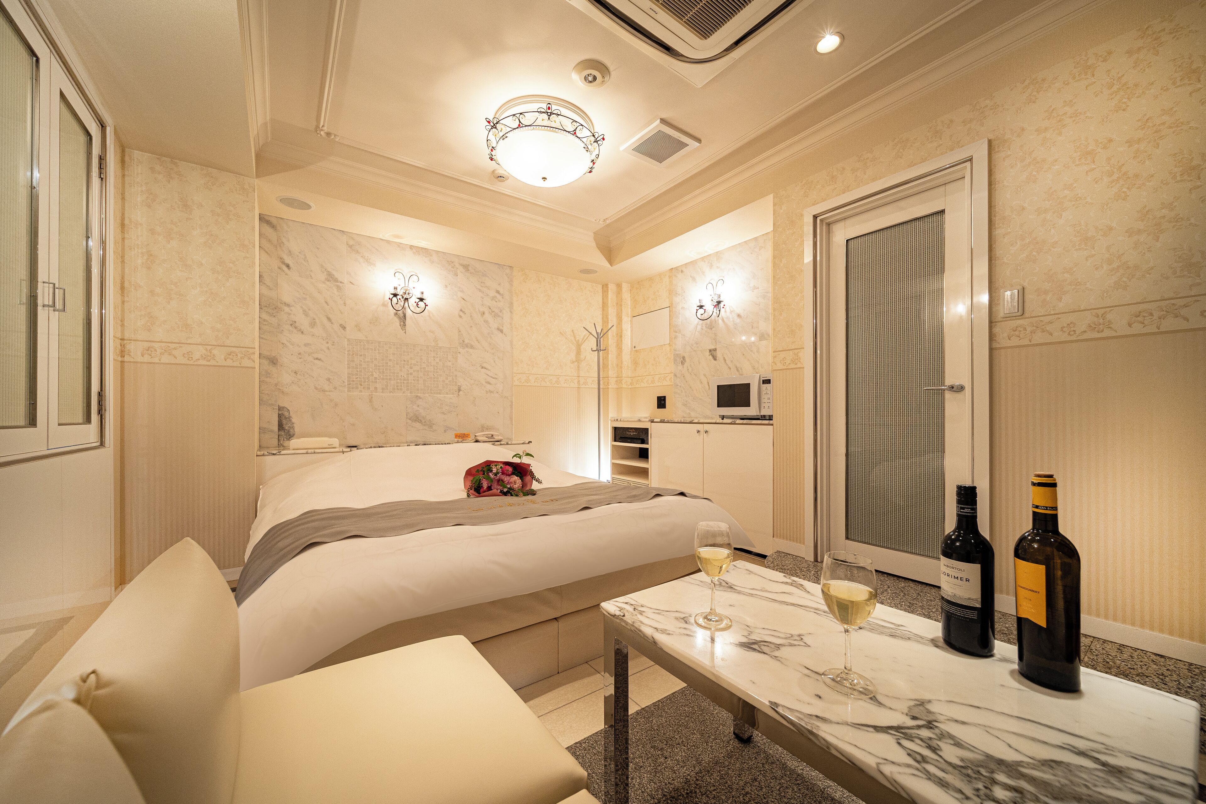 A hotel room with a bed, a sitting area, a marble table with wine bottles, and a mirror.