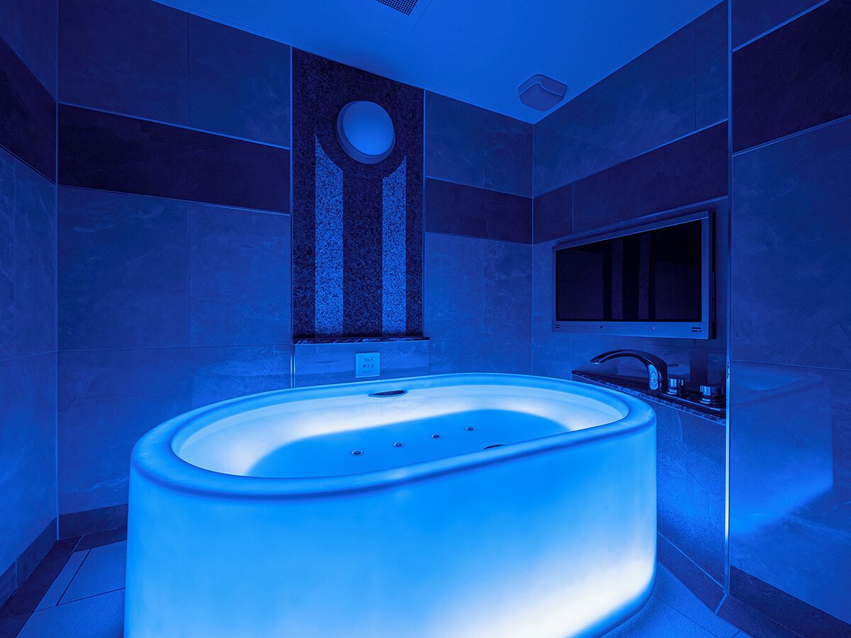 A modern bathroom with a large, illuminated bathtub, a round mirror, and a sleek, dark-toned sink.