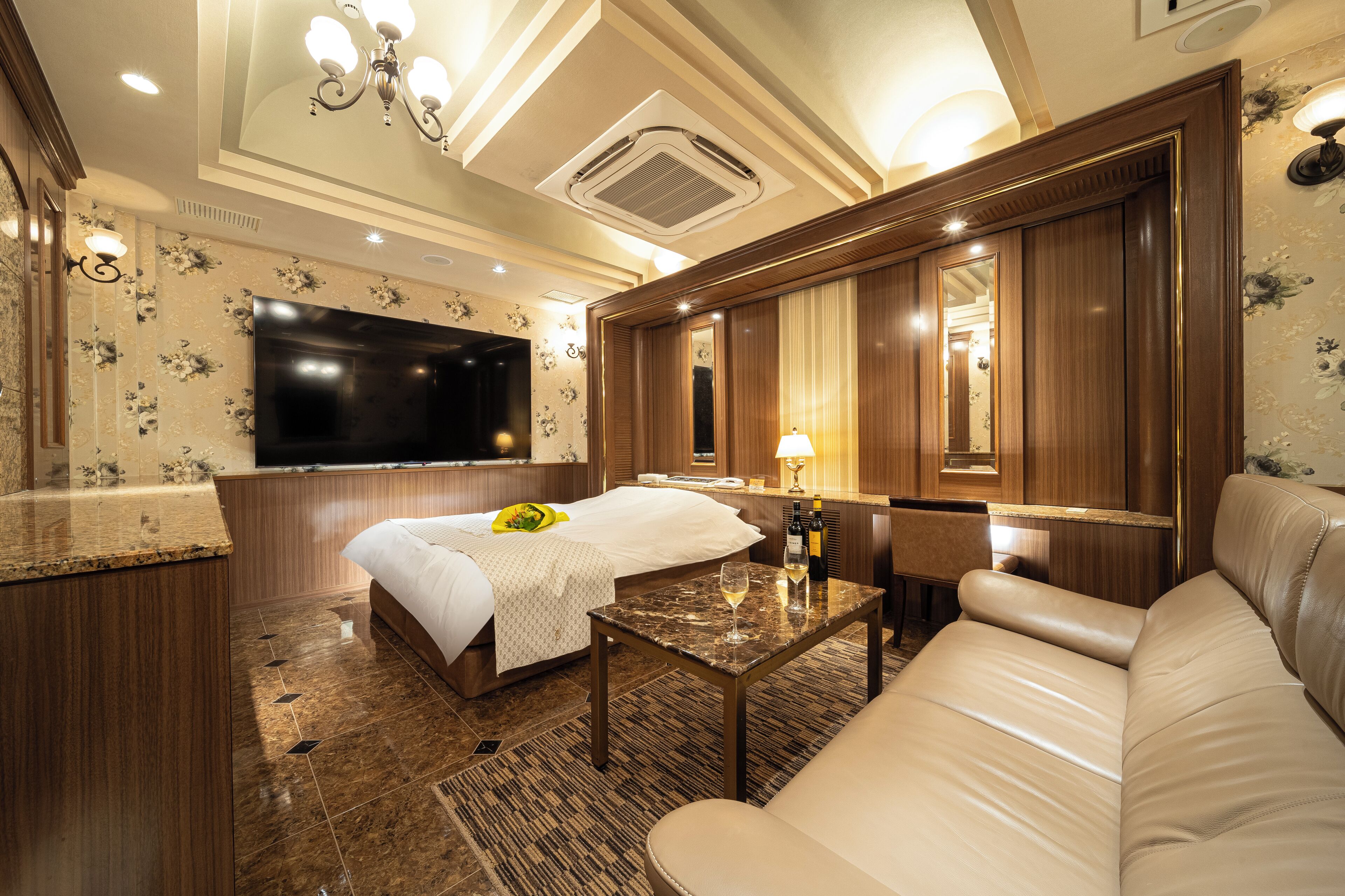 A hotel room with a large bed, a sofa, a TV, and a small table with a bottle and glass.