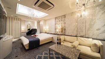 Quarto de hotel moderno com uma cama grande, um sofá, uma pequena mesa com garrafas e um candelabro.