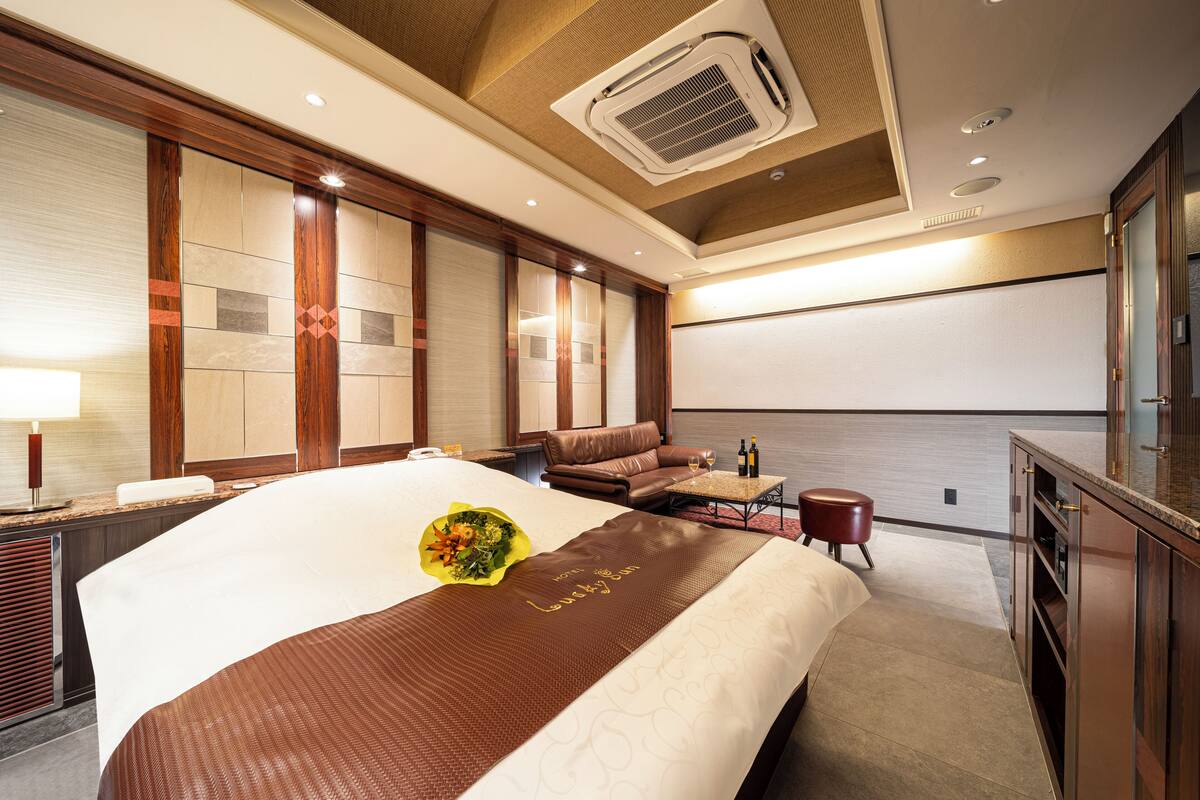 A hotel room with a large bed, a sofa, a small table, and a minibar.