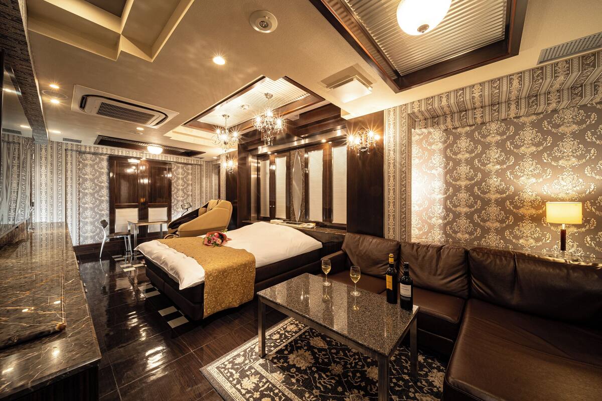 A modern hotel room with a large bed, a sofa, a coffee table, and a desk.
